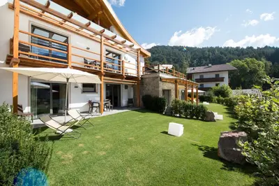 a house with a yard with chairs and an umbrella at Apartments Chalet Anna in Ortisei
