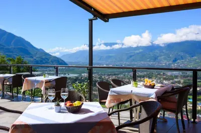 a restaurant with tables and chairs with mountains in the background at Hotel Panorama in Tirolo
