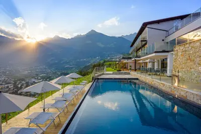 a pool with chairs and umbrellas next to a building at Hotel Panorama in Tirolo