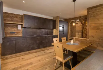 a dining room with a wooden table and a kitchen at Waidacherhof Apartments in Braies