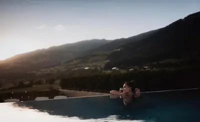 a woman sitting in a swimming pool with a mountain at Hotel Solvie in Falzes