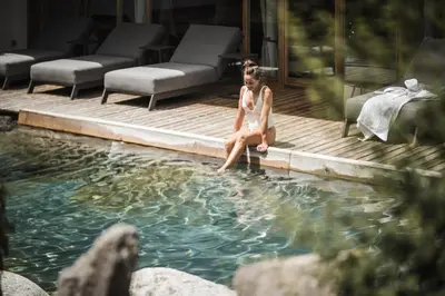 a woman sitting on the edge of a swimming pool at Hotel Lanerhof active/spa/balance in San Lorenzo di Sebato