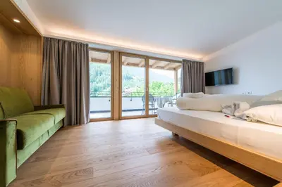 a bedroom with a bed and a couch and glass doors at Hotel Taufers in Molini di Tures