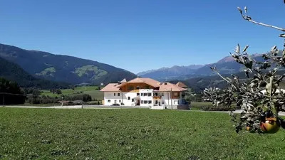 a large white house in a field with mountains in the background at Residence Stefansdorf in Brunico