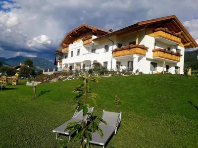 a building on a hill with chairs in the grass at Residence Stefansdorf in Brunico