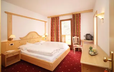 a bedroom with a bed and a desk and a window at Naturhotel Waldheim in Anterivo