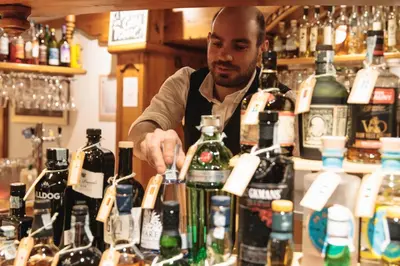 a man standing behind a counter with bottles of liquor at Hotel Belvedere in San Martino di Castrozza