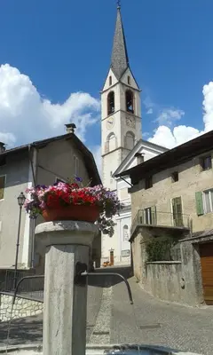 a church with a clock tower and a flower pot at Da Rinota in Alta Val di Non in Malosco