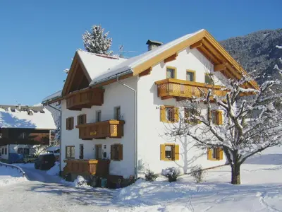 a white building with wooden balconies in the snow at Appartements Wiesenheim in Rasun di Sopra
