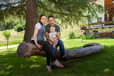a man and a woman holding a baby sitting on a log at Albergo Lozen in Canale San Bovo
