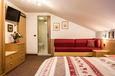 a bedroom with a red couch and a bathroom at Hotel Sonne Sole in Vigo di Fassa