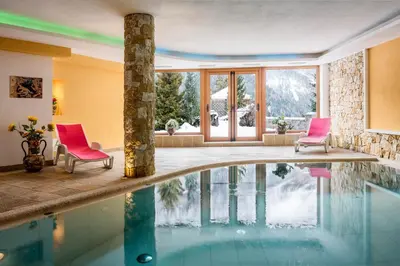 a pool in a house with two pink chairs and a table at Hotel Sonne Sole in Vigo di Fassa
