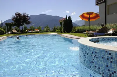 a swimming pool with an umbrella and a person sitting under an umbrella at Feldhof Schenna in Schenna