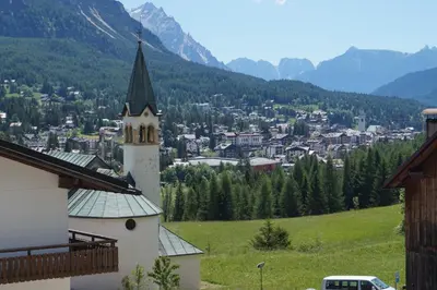 a church with a steeple on a hill with a town at Cadin Apartment in Cortina dʼAmpezzo