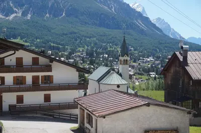 a small white church with a steeple in front of a mountain at Cadin Apartment in Cortina dʼAmpezzo