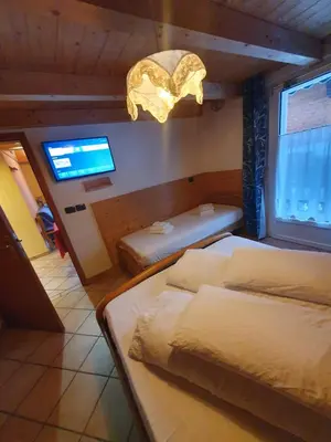 a bedroom with two beds and a tv and a window at casa claudio-APPARTAMENTI IN CENTRO in Campitello di Fassa