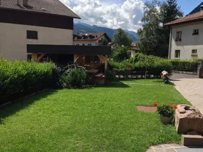 a yard with a house and green grass and flowers at Appartamento Rose Di Bosco in Predazzo