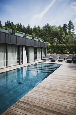 a house with a swimming pool next to a wooden deck at Nancy's Holiday Homes Dolomites in Rasùn di Sotto