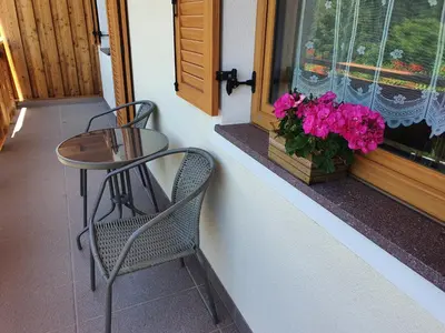 a table and a chair on a balcony with pink flowers at Mesnerhof in Lauregno