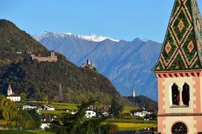 a clock tower in a town with mountains in the background at Angerburg Blumenhotel in Appiano sulla Strada del Vino