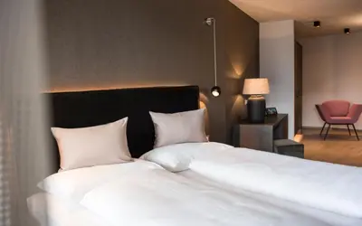 a bedroom with a bed with white sheets and a chair at Hotel - Appartements Schmied Hans in Schenna