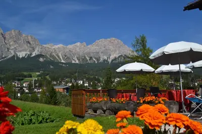 a table with umbrellas and flowers with mountains in the background at Hotel Villa Nevada in Cortina dʼAmpezzo