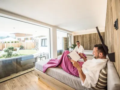 a man laying in a chair reading a book in a bedroom at Apartment Sella in Siusi