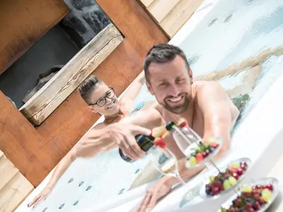 two men in a bath tub with a bottle of wine at Apartment Sella in Siusi