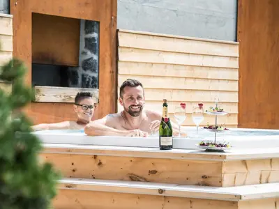 two men in a bathtub with a bottle of wine at Apartment Sella in Siusi