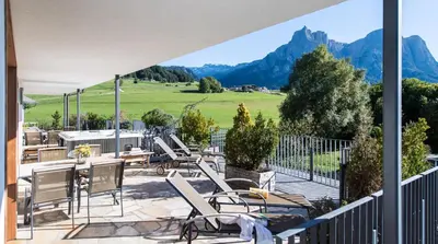 a patio with chairs and tables with mountains in the background at Apartments Elisir in Castelrotto