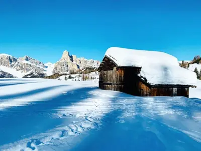 a barn covered in snow with mountains in the background at Nei Y Suredl NeveSole in Corvara in Badia