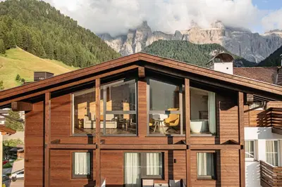 a house with windows and mountains in the background at Garni Hotel Miara - Your Dolomites Home in Selva di Val Gardena