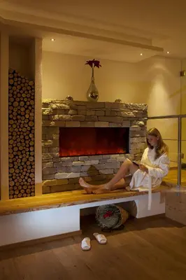 a woman sitting on a bench in front of a fireplace at Garni Hotel Miara - Your Dolomites Home in Selva di Val Gardena