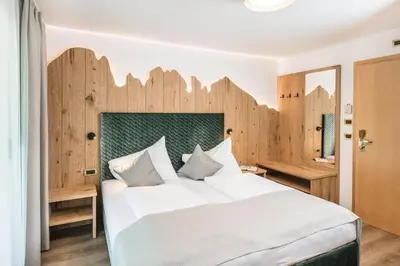 a bedroom with a large bed with a wooden headboard at Garni Hotel Miara - Your Dolomites Home in Selva di Val Gardena