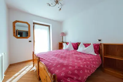 a bedroom with a bed with pink sheets and a mirror at Appartamenti Majon Ladina in Vigo di Fassa