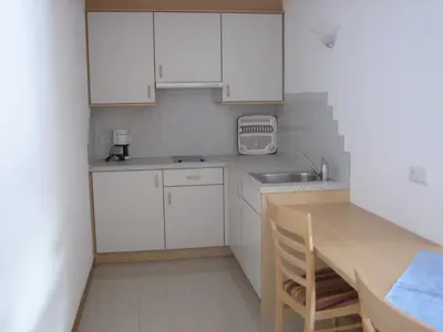 a small kitchen with white cabinets and a wooden table at Garni - Appartement Neumairhof in Rasun di Sopra