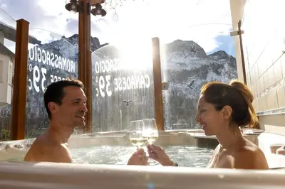a man and woman in a hot tub with a glass of wine at Hotel San Marco in Passo San Pellegrino