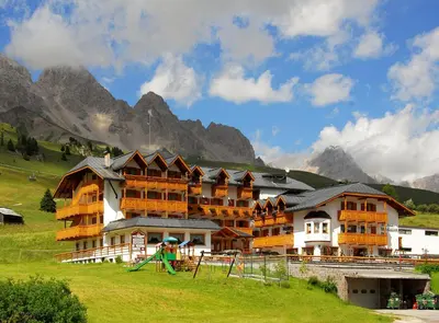 a large building with a playground in front of a mountain at Hotel San Marco in Passo San Pellegrino