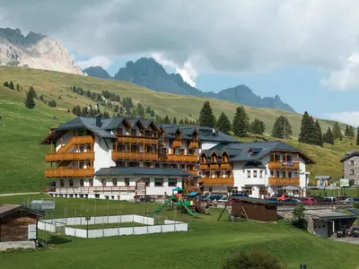 a large building with a playground in front of a mountain at Hotel San Marco in Passo San Pellegrino