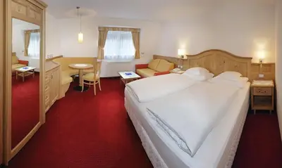 a bedroom with a large white bed and a living room at Hotel Ingram in Selva di Val Gardena