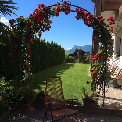 an arch with roses and a chair in a yard at Hotel Garni Paler in Tirolo