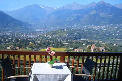a table and chairs on a balcony with a view of mountains at Schwarzplatterhof in Merano