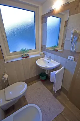 a bathroom with a sink and a toilet and a window at Hotel La Molinella in Soraga