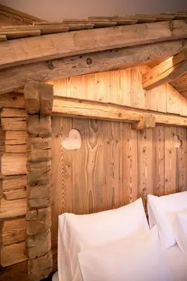 a bedroom with a wooden wall and a bed with white sheets at Agriturismo Malga Piè in Soraga