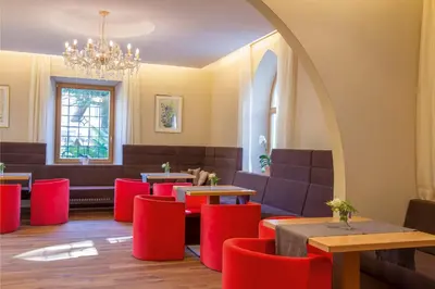 a restaurant with red chairs and tables and a chandelier at Hotel Sonnenhof in Merano