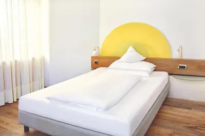 a bedroom with a white bed with a yellow headboard at Hotel Sonnenhof in Merano