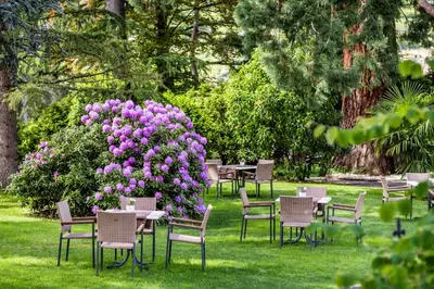 a group of tables and chairs in a park with purple flowers at Hotel Sonnenhof in Merano