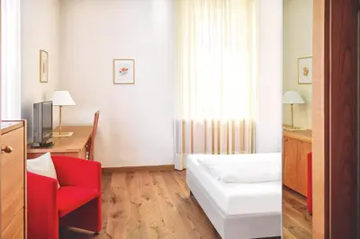 a hotel room with a bed and a red chair at Hotel Sonnenhof in Merano