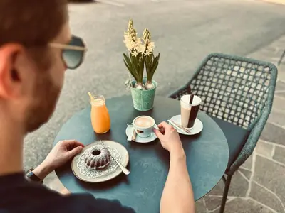 a man sitting at a table with a doughnut and coffee at Residence Neuhäuslhof in Merano