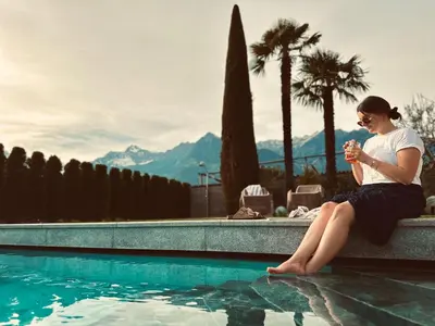 a woman sitting on a ledge next to a swimming pool at Residence Neuhäuslhof in Merano